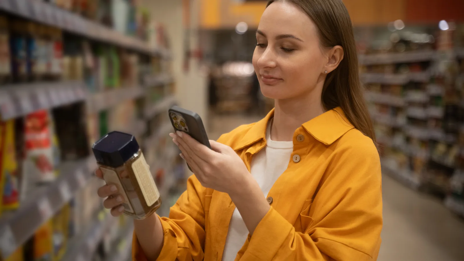 A shopper scanning a product in a supermarket aisle with her phone.