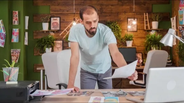 A designer leaning over a studio table reviewing printed proofs.