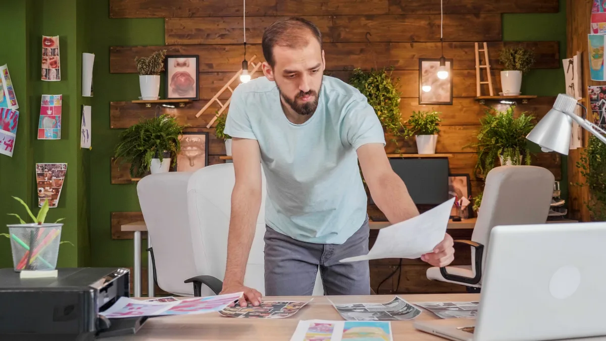 A designer leaning over a studio table reviewing printed proofs.
