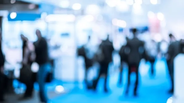 Visitors moving between exhibitor stands in a busy trade exhibition hall.