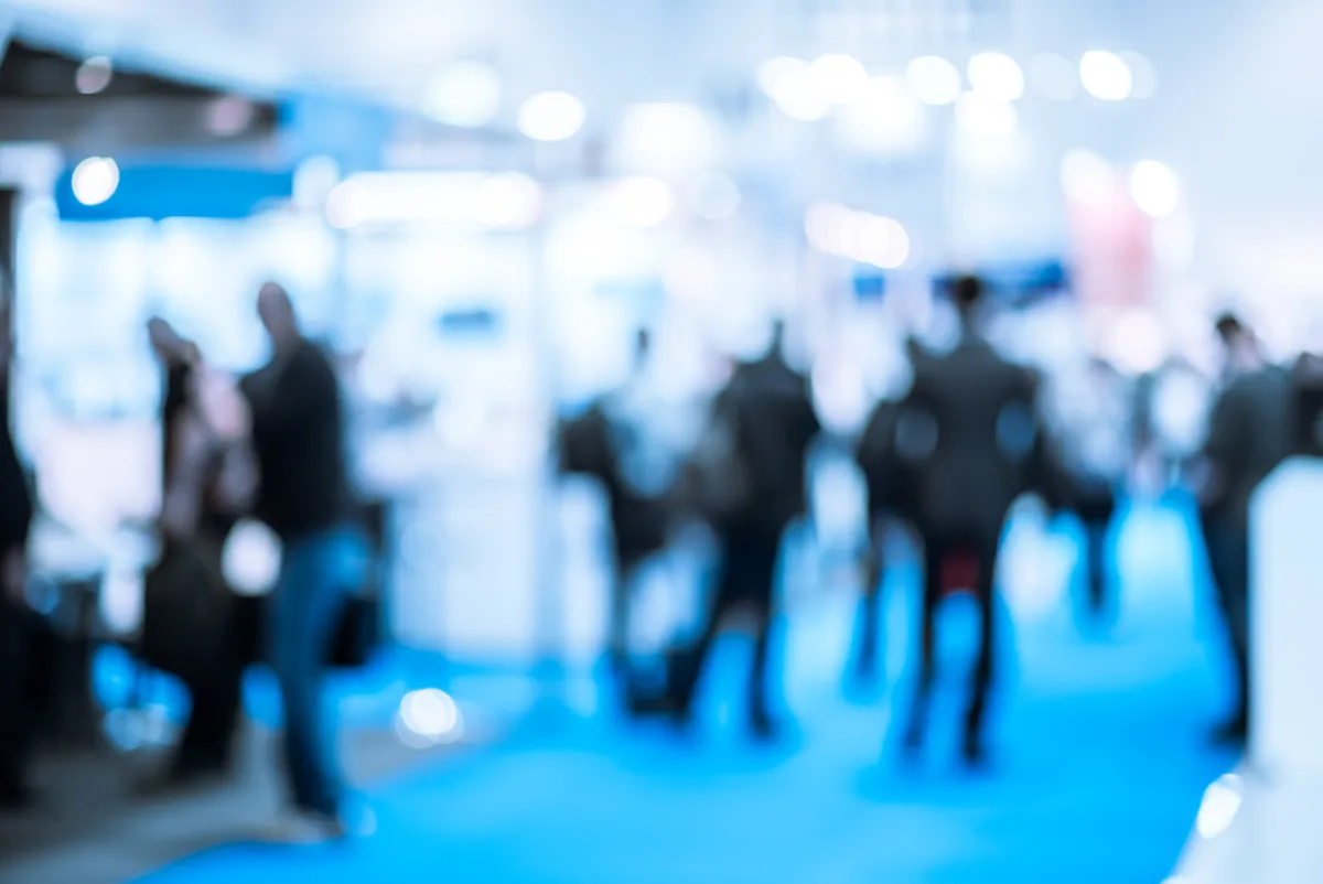 Visitors moving between exhibitor stands in a busy trade exhibition hall.