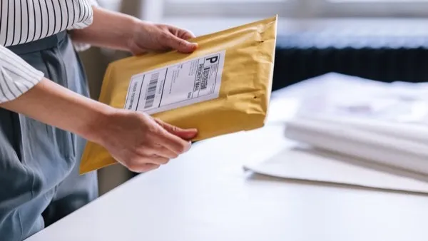 Hands taping up a cardboard box with a printed label, ready for shipping.