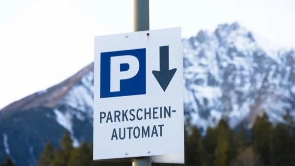 A German Parkscheinautomat parking sign on a pole against snow-covered mountains.